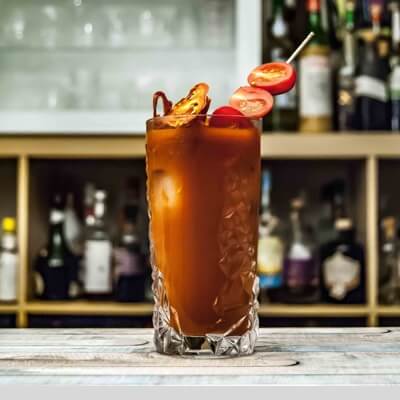 a orange-coloured alcoholic drink in a long trasnparent glass with baby tomatoes on top