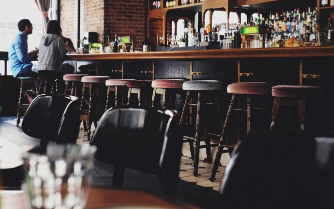 a picture of a bar with multiple bar chairs and two customers chatting